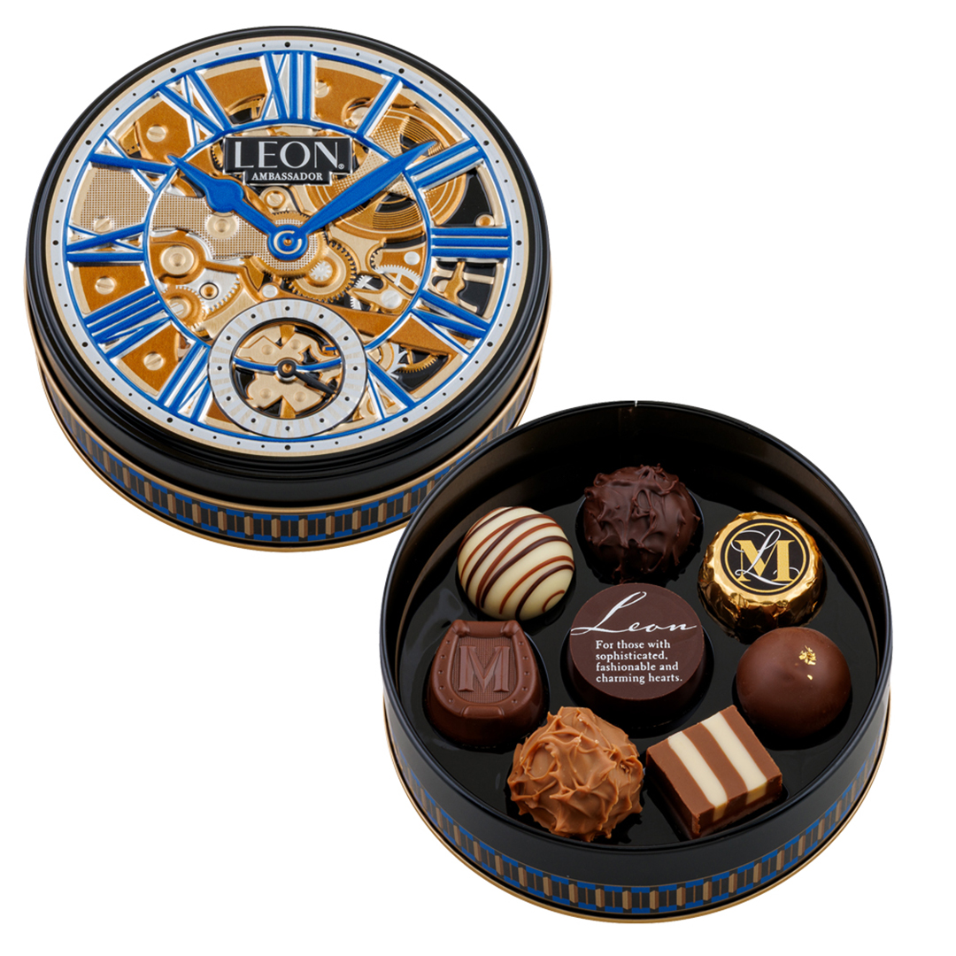 Round tin of assorted chocolates, featuring a decorative lid with clock design. Chocolates have varied textures and patterns.