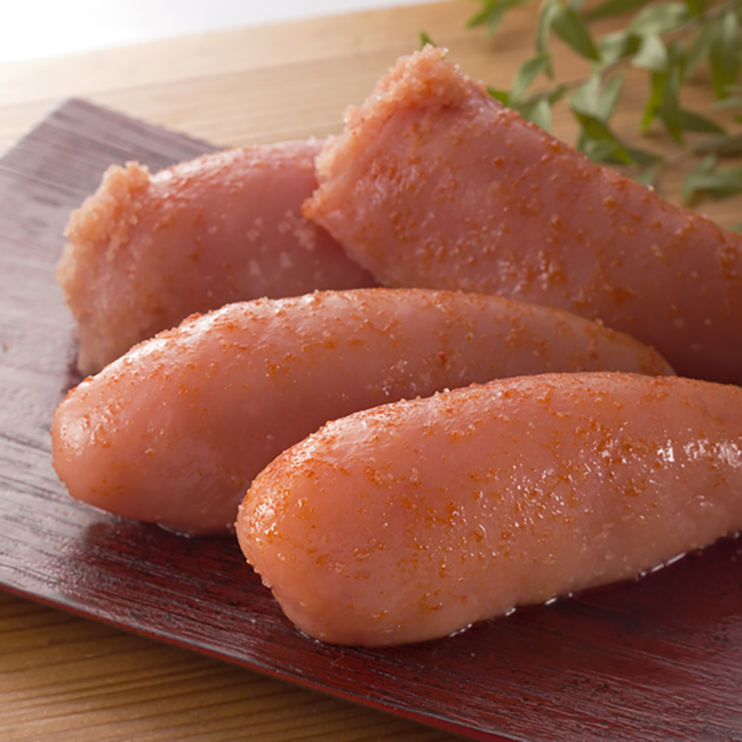 Four seasoned cod roe pieces on a wooden plate, with a green garnish in the background.