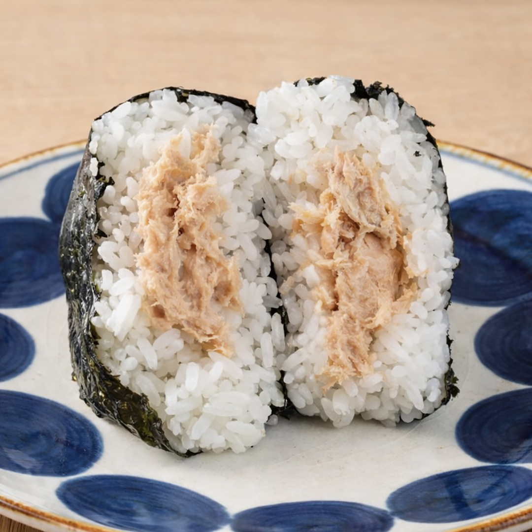 A halved onigiri filled with tuna, wrapped in seaweed, placed on a plate with a blue and white pattern.