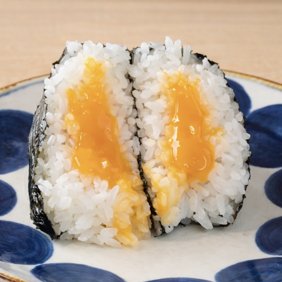 Halved onigiri with a soft, runny egg yolk center on a white plate with blue designs. Wrapped in nori, displaying a mix of textures.