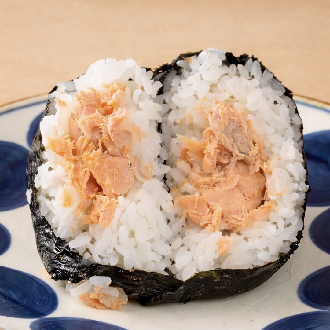 Onigiri with salmon filling, wrapped in seaweed, cut in half and served on a plate with a blue dot pattern.