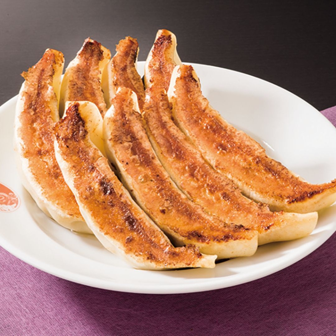 A plate of eight crispy, golden-brown gyoza dumplings on a white plate, set on a purple cloth.