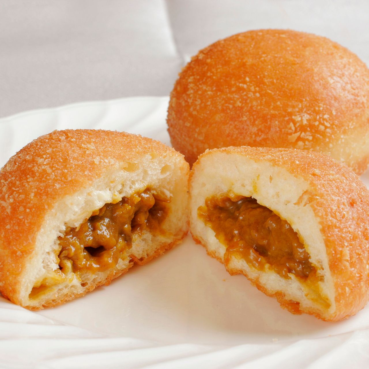 Two deep-fried curry buns on a plate, one cut open to reveal a savory curry filling.