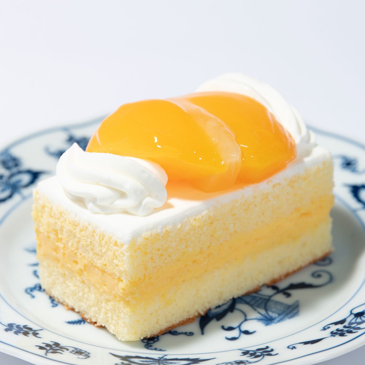 Slice of sponge cake with cream layers and peach slices, served on a blue-patterned plate.
