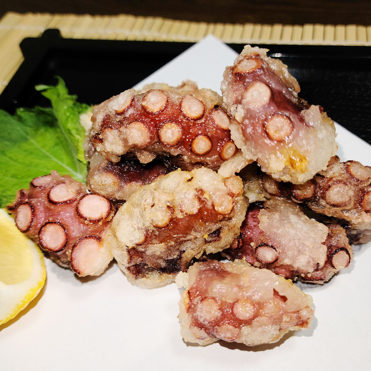 Fried octopus pieces served on a white plate with lettuce and a lemon wedge on the side.
