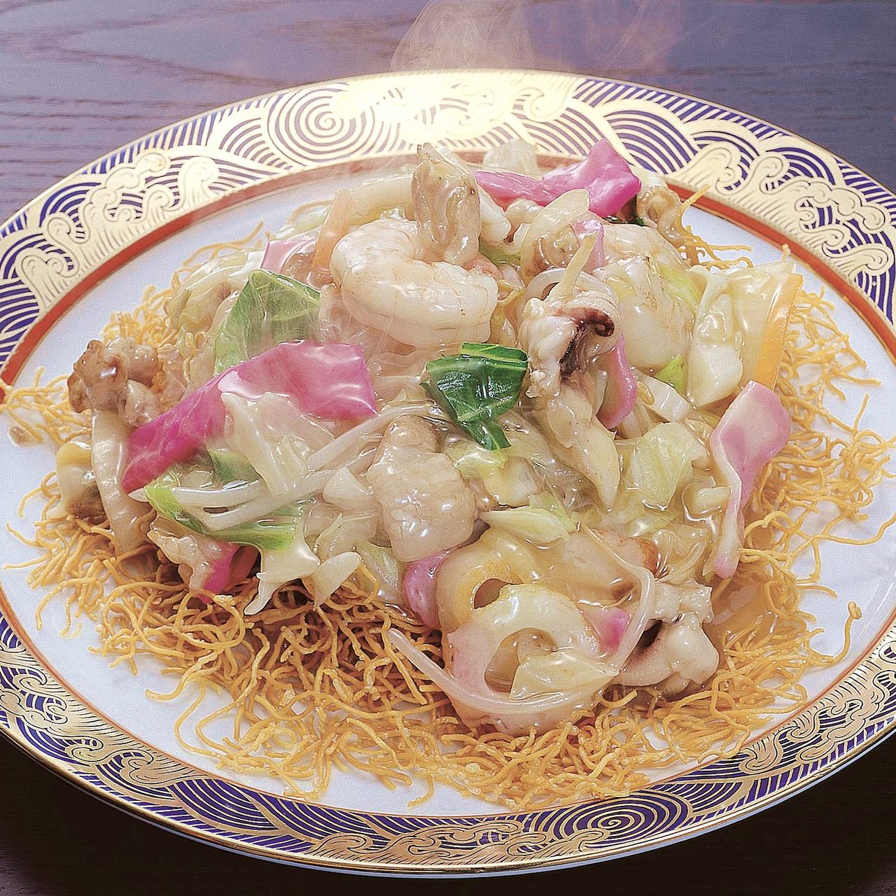 Plate of crispy fried noodles topped with seafood, vegetables, and a creamy sauce on an ornate dish.