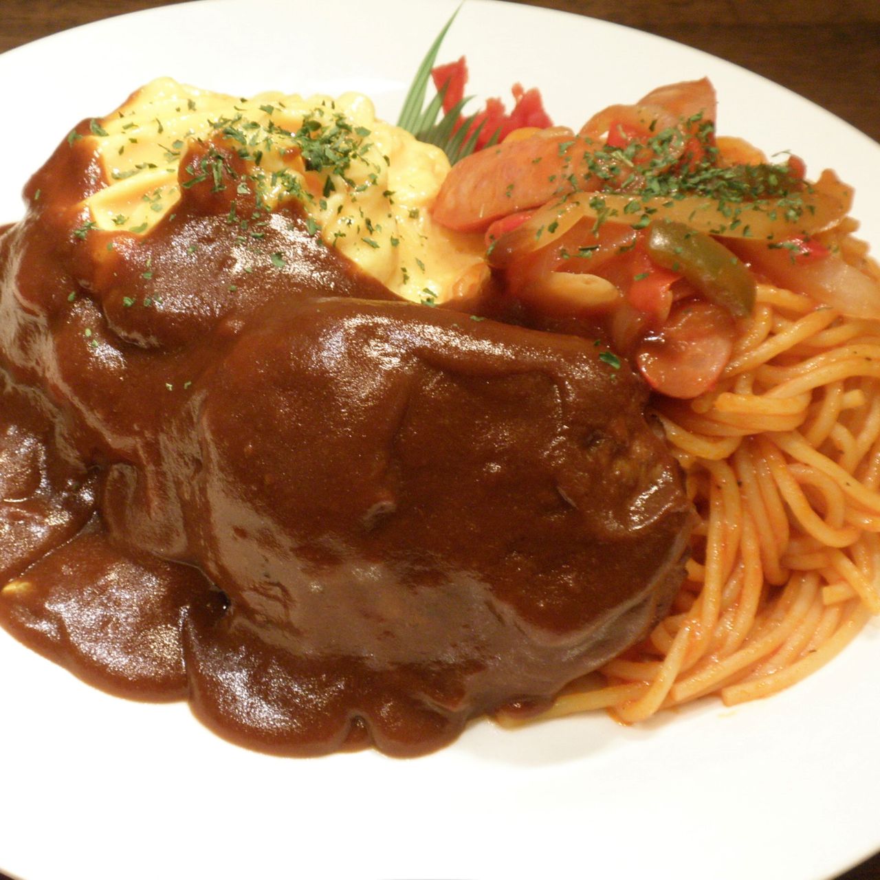 Plate with hamburger steak in rich brown sauce, creamy mashed potatoes, and spaghetti with tomato sauce, garnished with herbs.