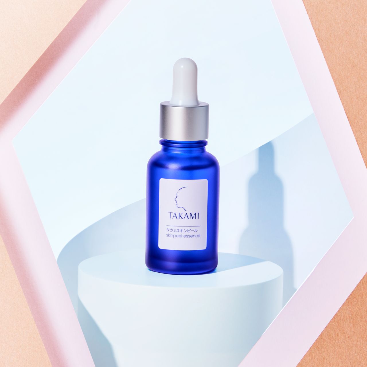 A blue Takami skincare serum bottle with a dropper, placed on a white pedestal against a geometric background.