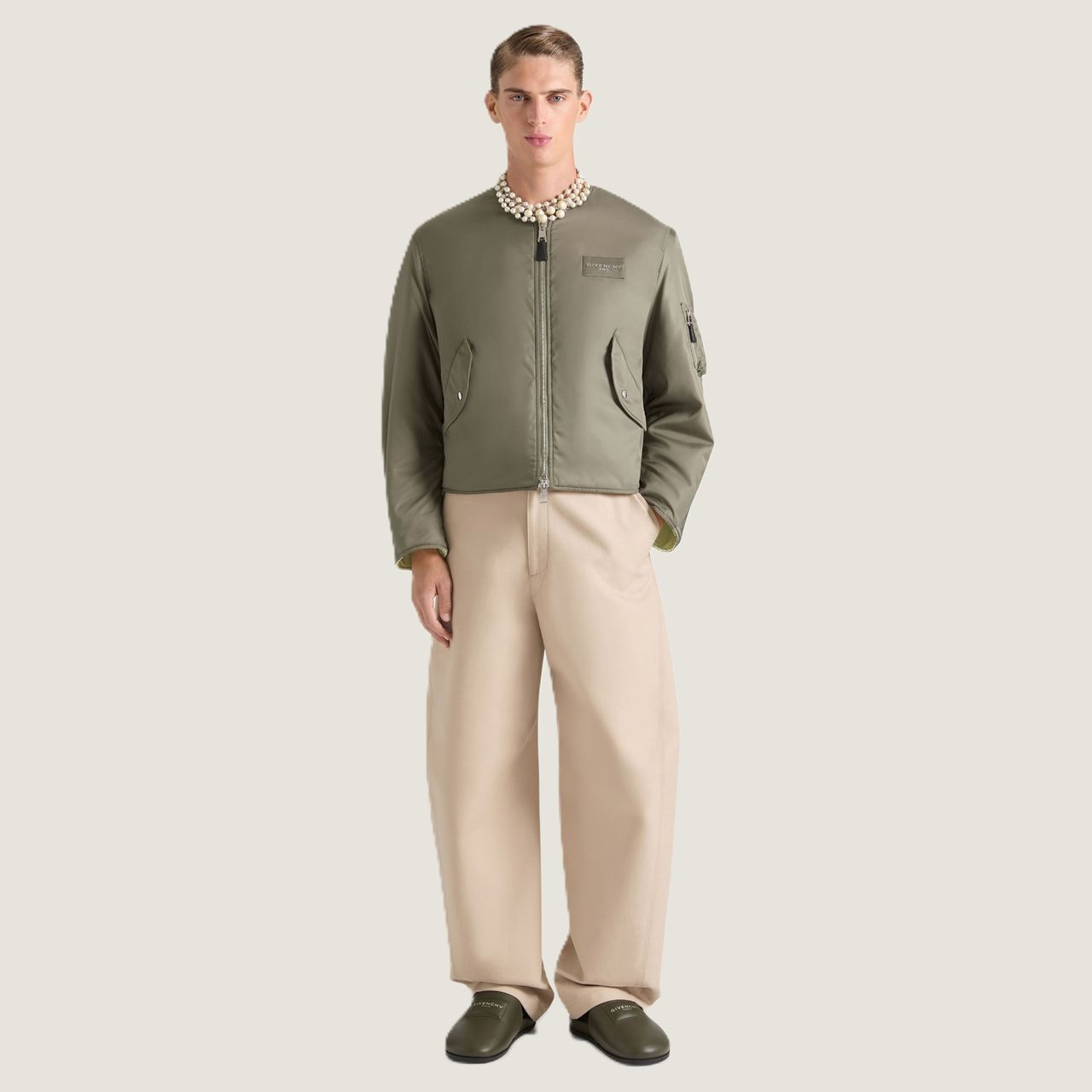 Person wearing a green bomber jacket, beige wide-leg pants, and green shoes, standing against a plain background.