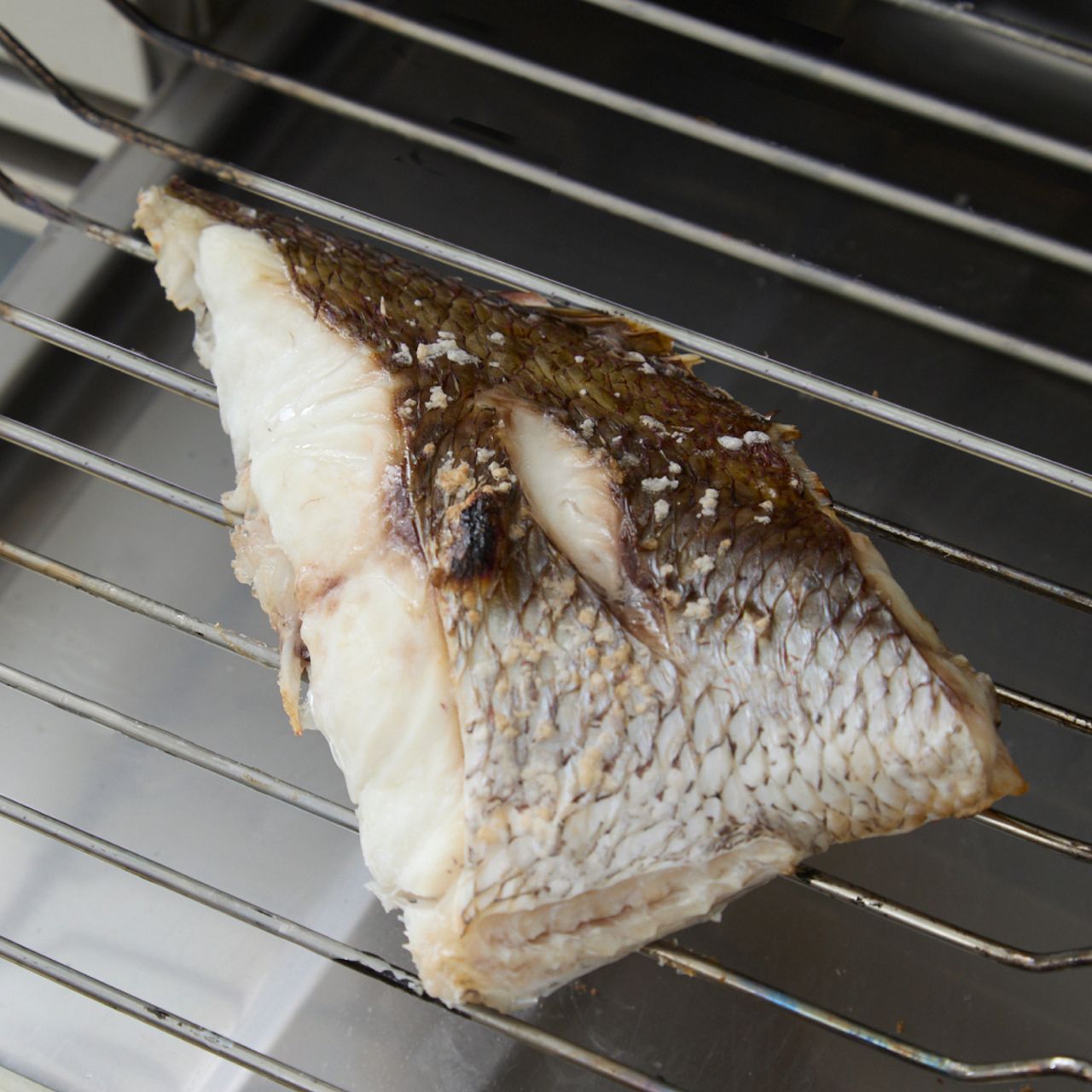 Grilled fish portion on a metal rack, showing crispy skin and tender white flesh.