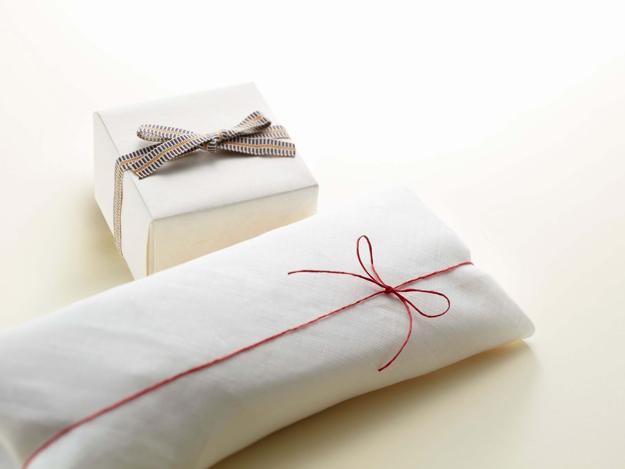 A white gift box with a striped bow and a wrapped package tied with red string on a light background.