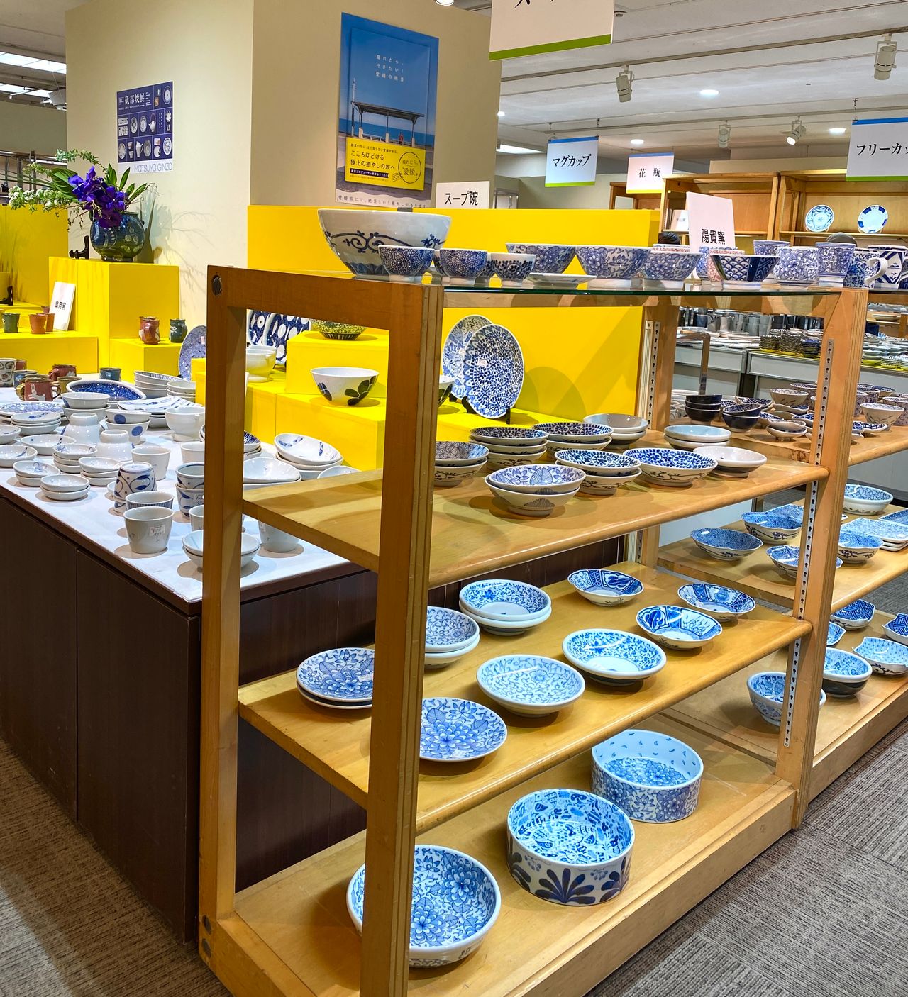 Shelves of blue and white ceramic bowls in a store, with a variety of patterns and designs, surrounded by bright yellow displays.