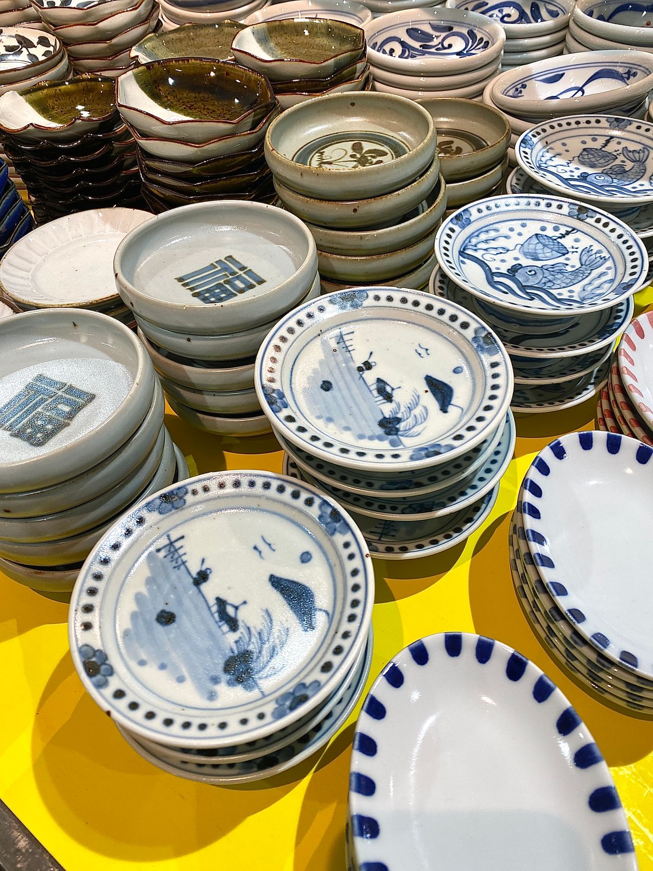 Stacks of decorative ceramic plates with various blue patterns on a bright yellow surface.