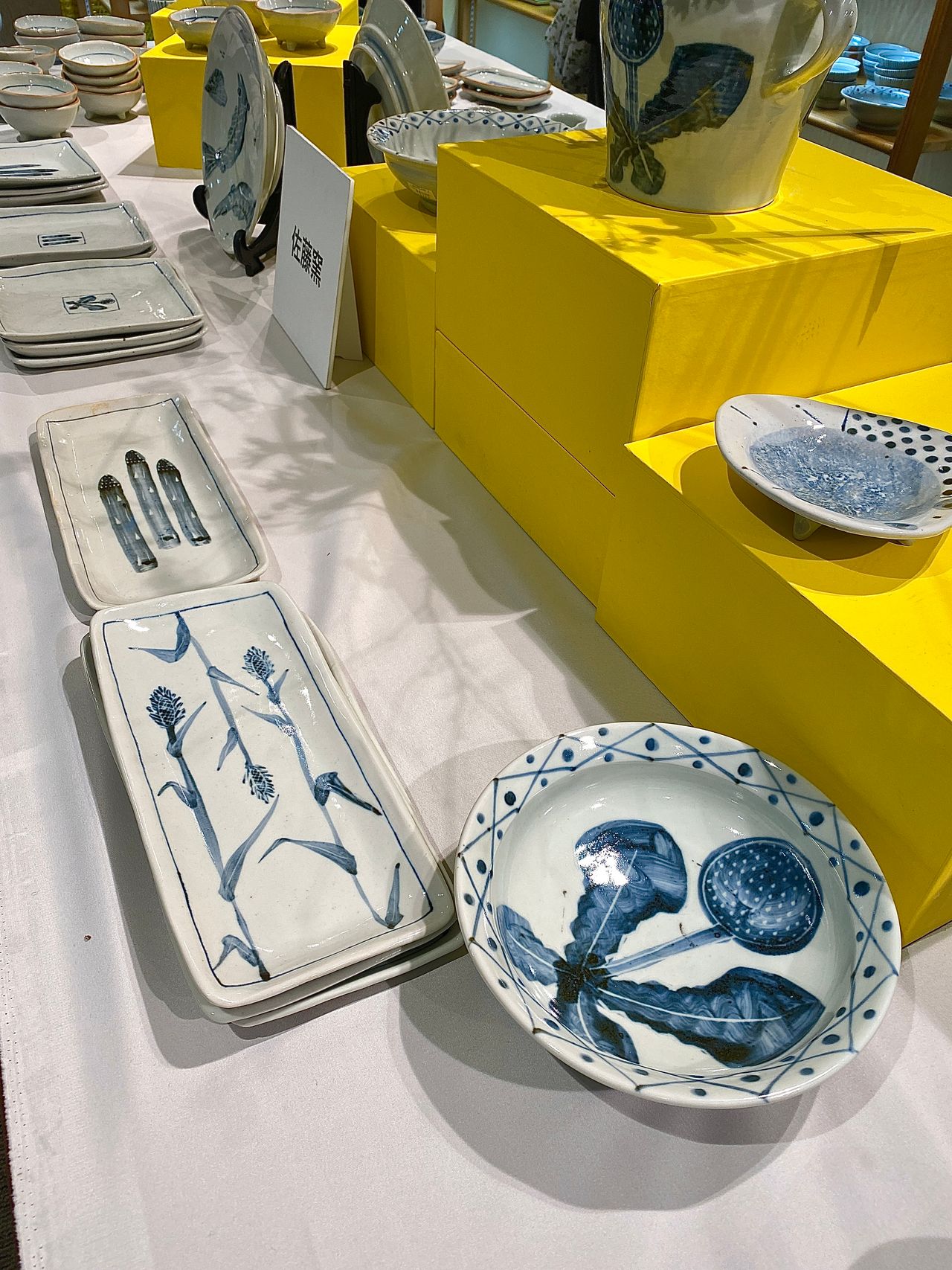 A display of white ceramic tableware with blue botanical designs on a white and yellow shelf setup.