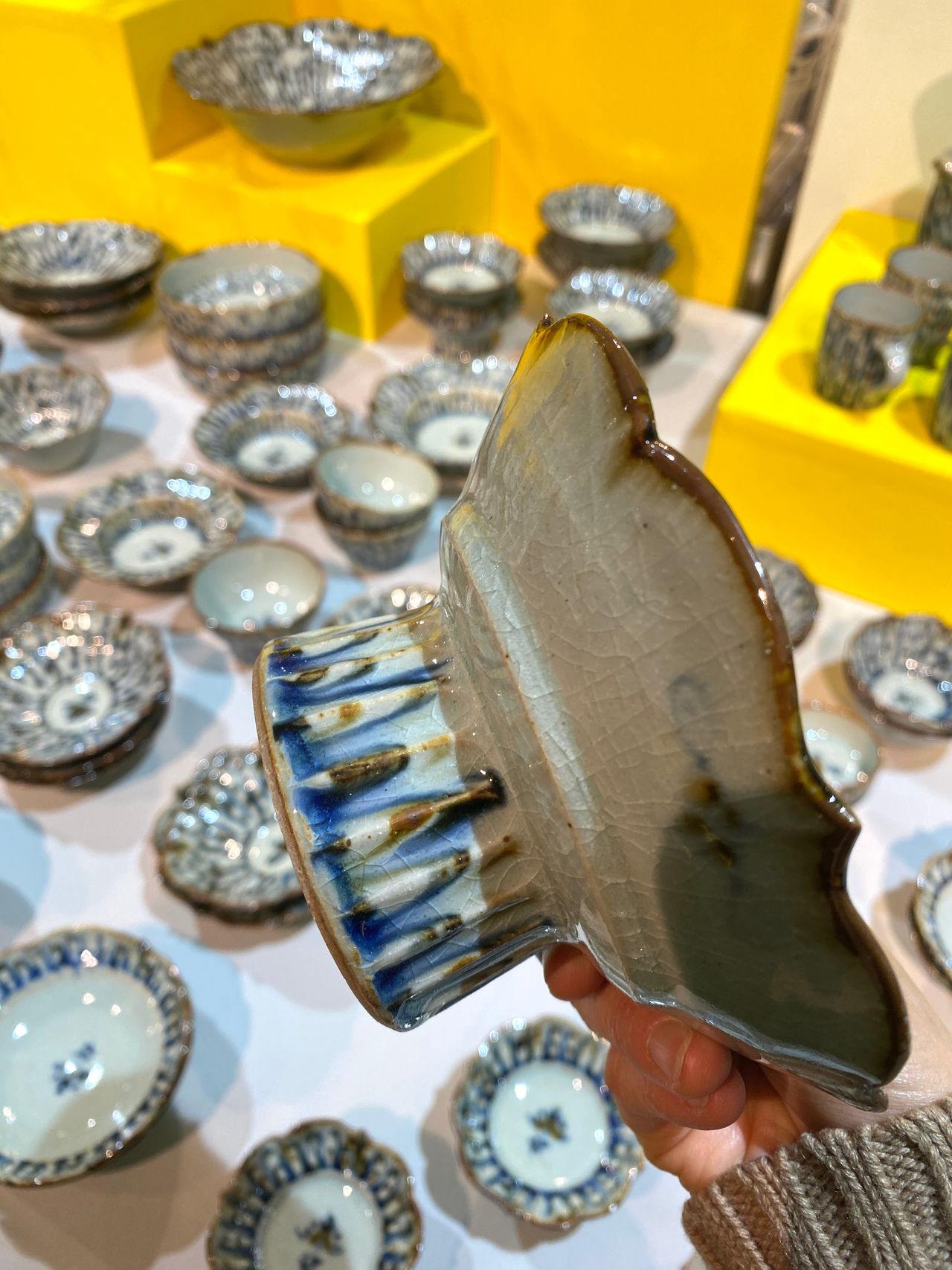 Hand holding a uniquely shaped ceramic piece, surrounded by various blue and white patterned bowls on a table.