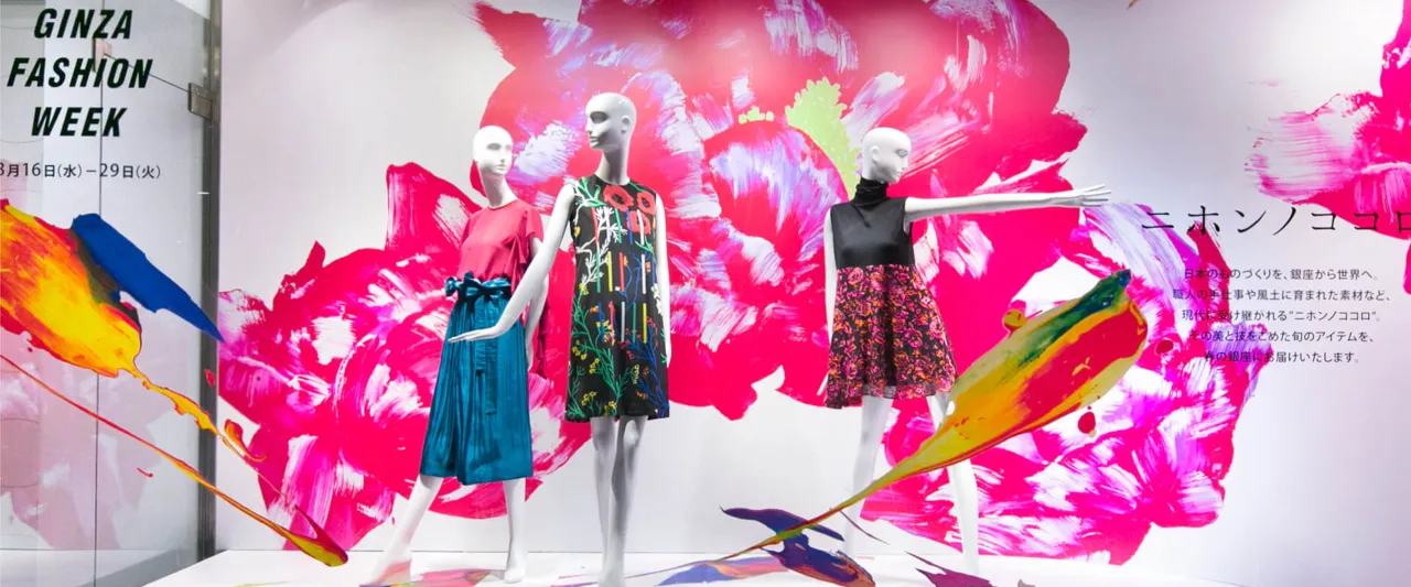 Mannequins in vibrant floral outfits displayed in front of a colorful, artistic backdrop at Ginza Fashion Week.