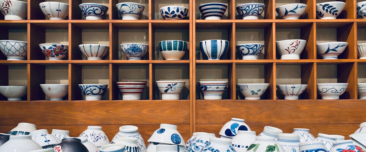 A wooden shelf displaying various ceramic bowls with intricate blue and white patterns. Additional bowls are stacked below.