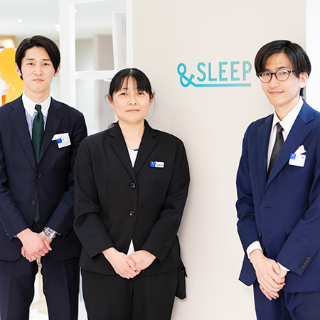 Three people in formal attire stand by a wall with the word "&SLEEP" on it. They are wearing name tags and smiling.