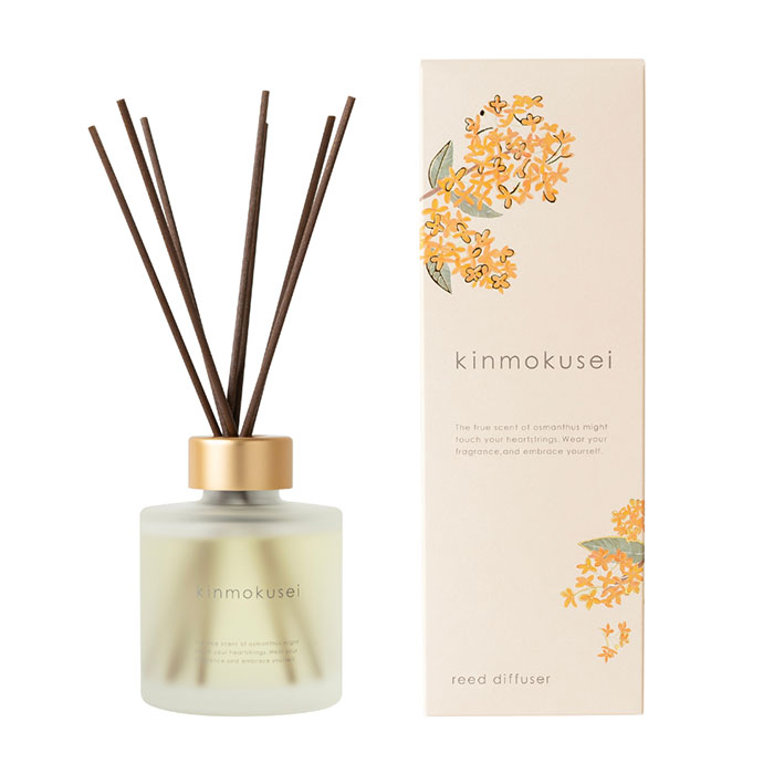 Reed diffuser with brown sticks in a frosted glass bottle, next to a box decorated with orange flowers and labeled "kinmokusei."